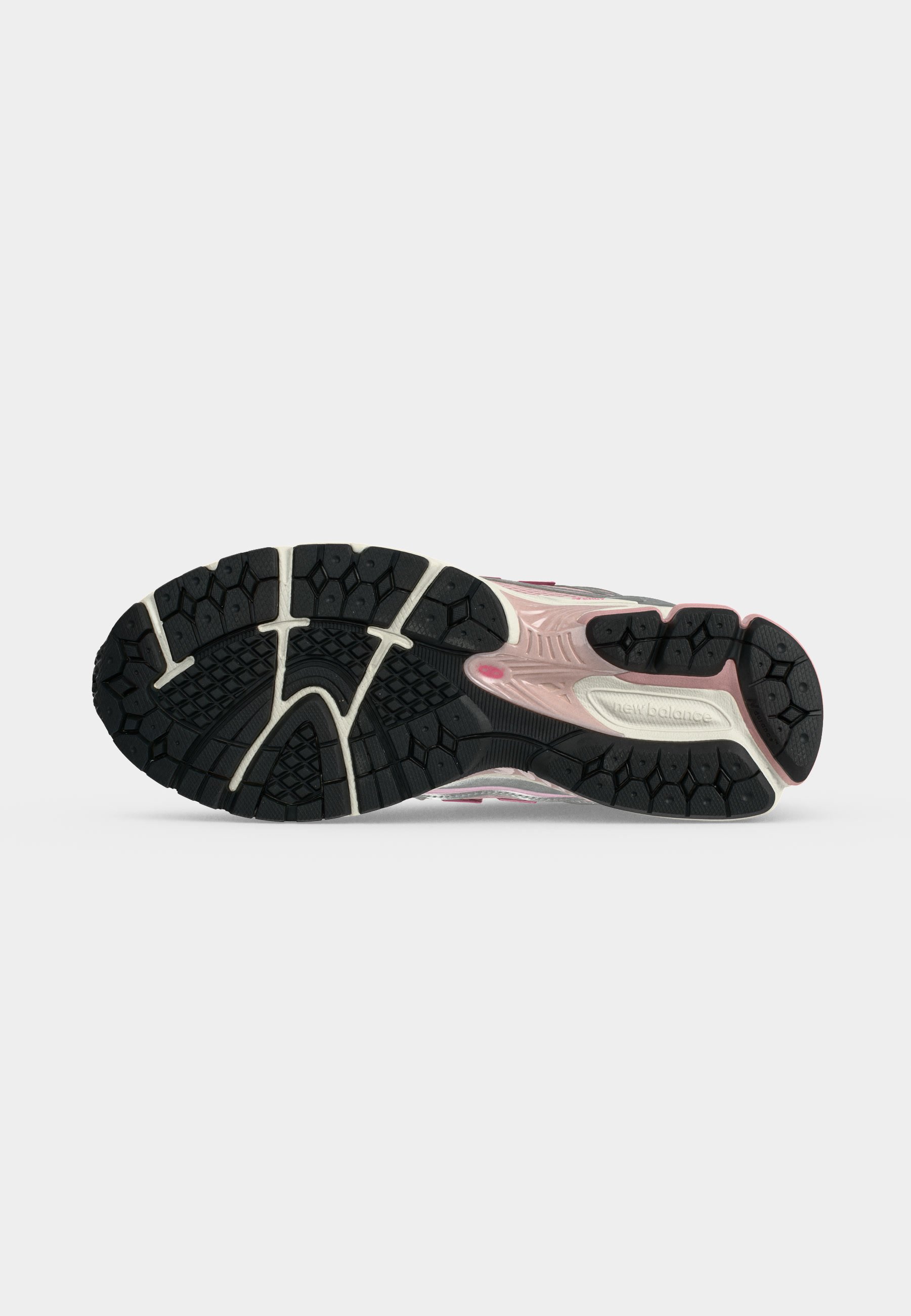 Suela de zapato con patrón de banda de rodadura en blanco y negro, detalle rosa en la entresuela y logotipo de New Balance sobre un fondo liso gris claro.