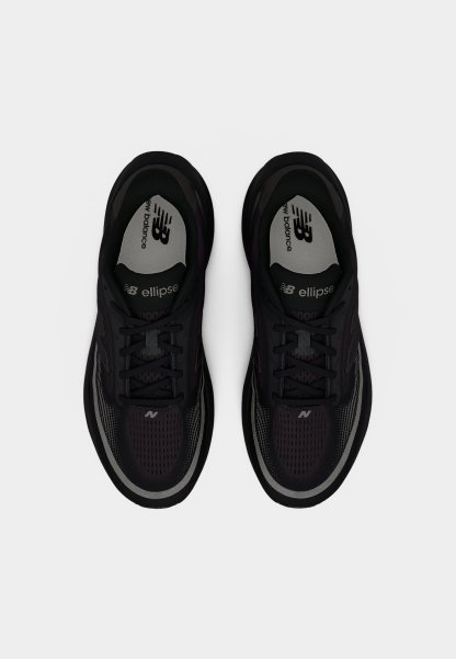 Zapatillas deportivas negras con parte superior de malla, diseño con cordones y suela de goma. Presentan detalles en gris y la marca "New Balance" en la plantilla.