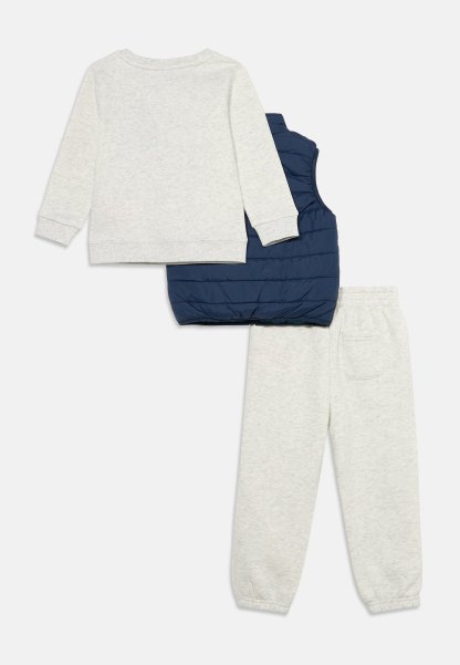 Conjunto de camisa de manga larga y pantalones gris claro con puños elásticos, combinado con un chaleco acolchado sin mangas azul marino.