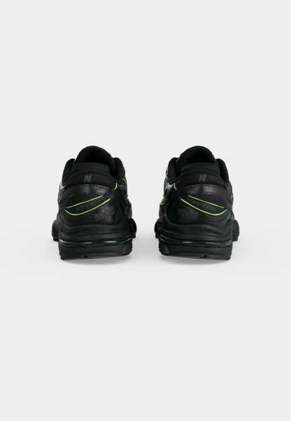 Par de zapatillas negras New Balance 1000 con detalles en verde neón, mostradas desde atrás sobre un fondo liso gris claro.
