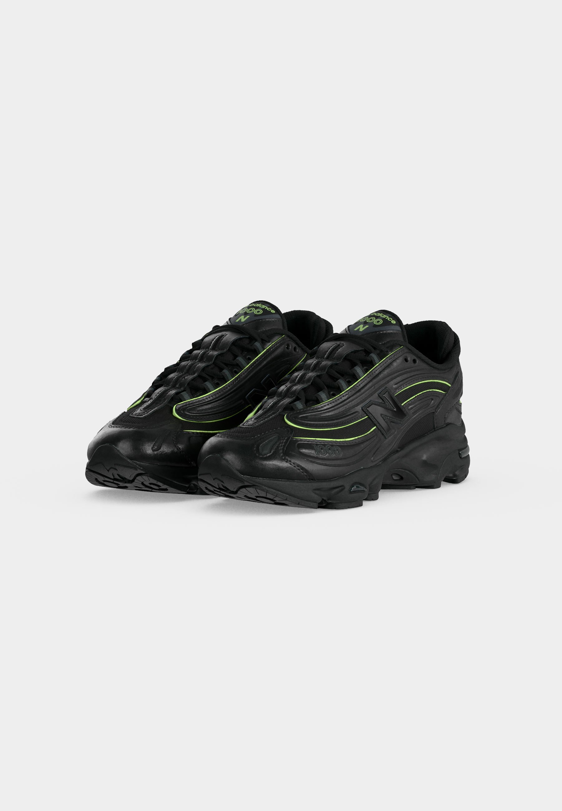 Par de zapatillas deportivas negras con detalles verdes y suelas gruesas, colocadas en ángulo para mostrar detalles frontales y laterales sobre un fondo claro y liso.