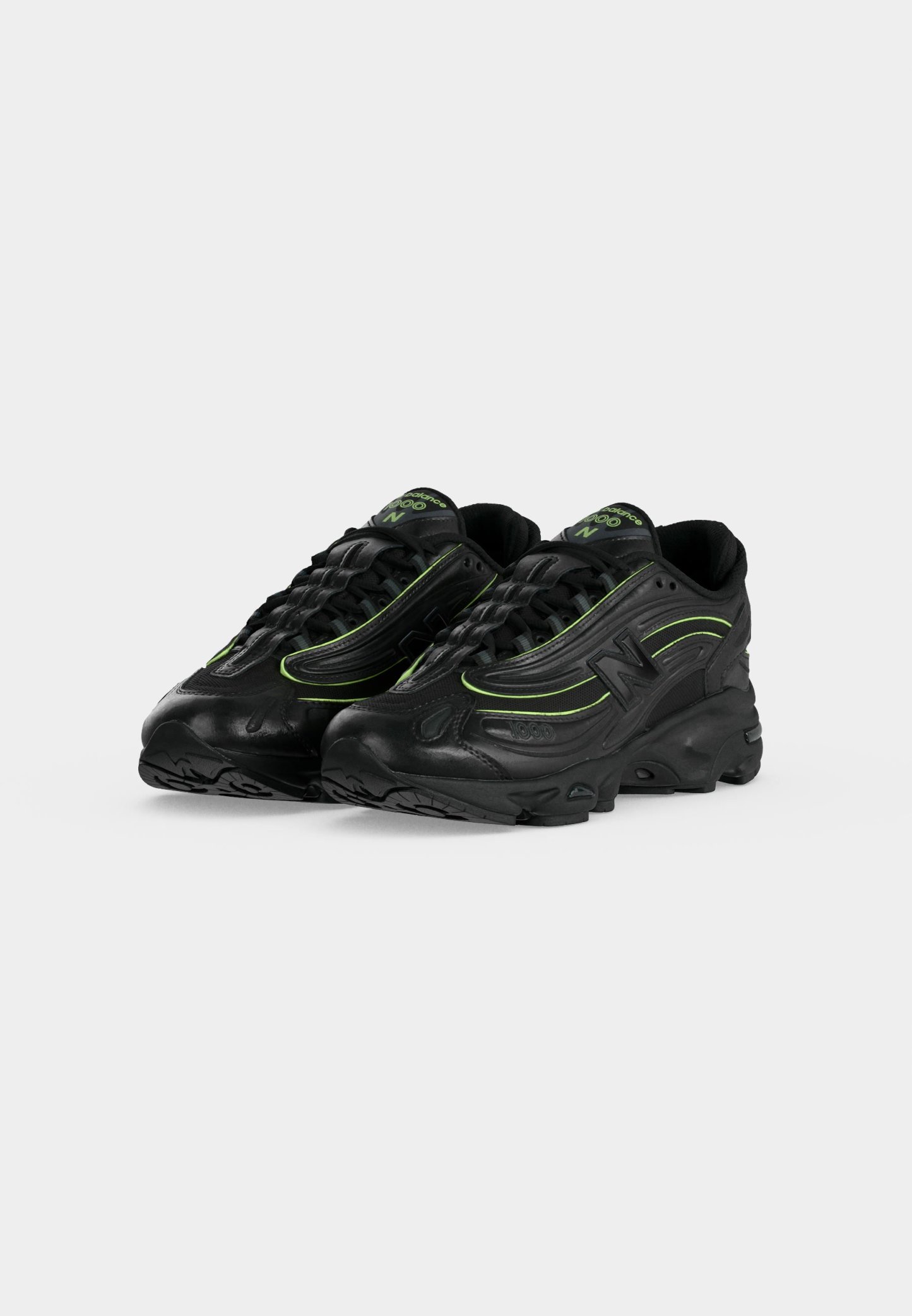 Par de zapatillas deportivas negras con detalles verdes y suelas gruesas, colocadas en ángulo para mostrar detalles frontales y laterales sobre un fondo claro y liso.