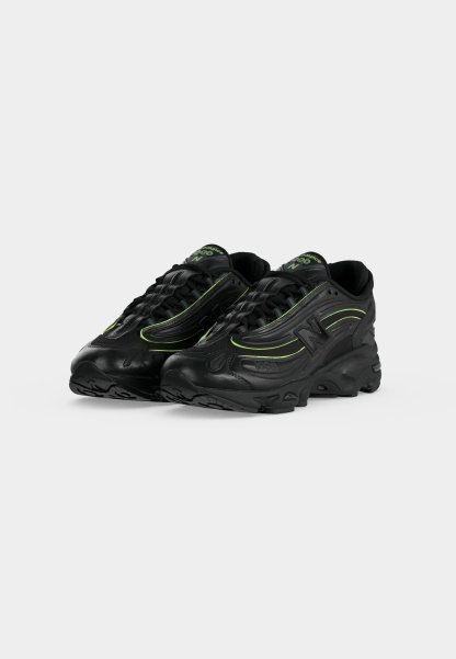 Par de zapatillas deportivas negras con detalles verdes y suelas gruesas, colocadas en ángulo para mostrar detalles frontales y laterales sobre un fondo claro y liso.