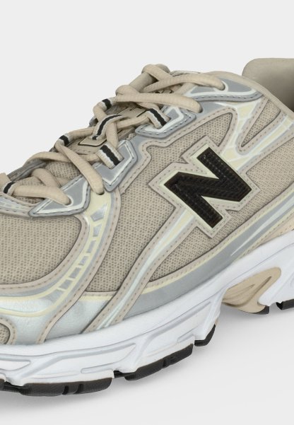 Zapatilla de running en beige y gris con logo "N" negro, cordones beige claro y suela blanca con detalles negros en la banda de rodadura.