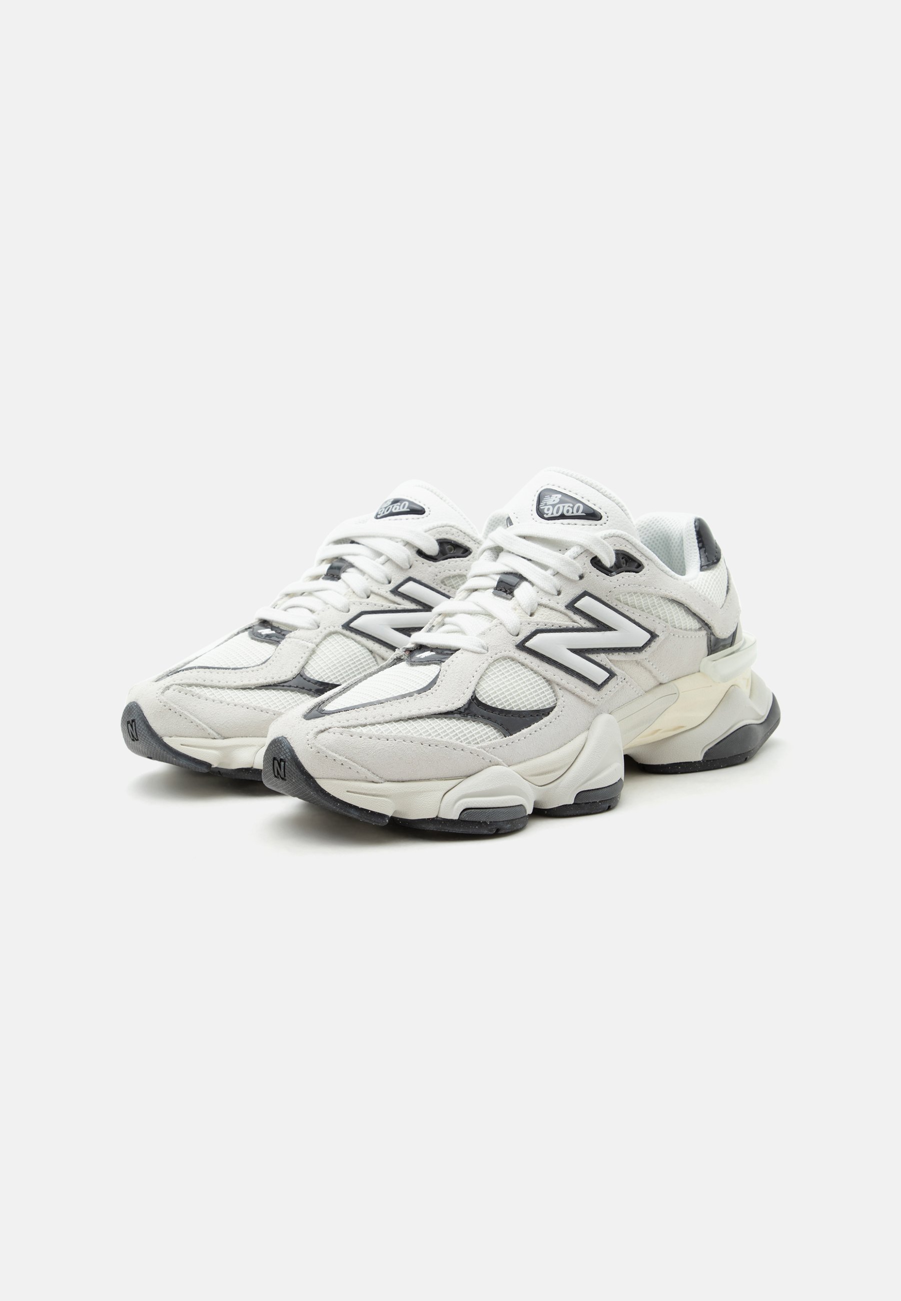 Zapatillas New Balance 9060 blancas y grises con paneles de malla y cuero, suelas gruesas y logo "N" en los laterales y las lengüetas.