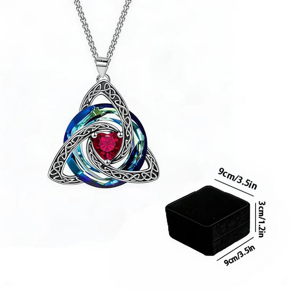 Silver Celtic knot triquetra pendant necklace with a blue and green iridescent circular background and a central red crystal, shown with a black jewelry box and size measurements.