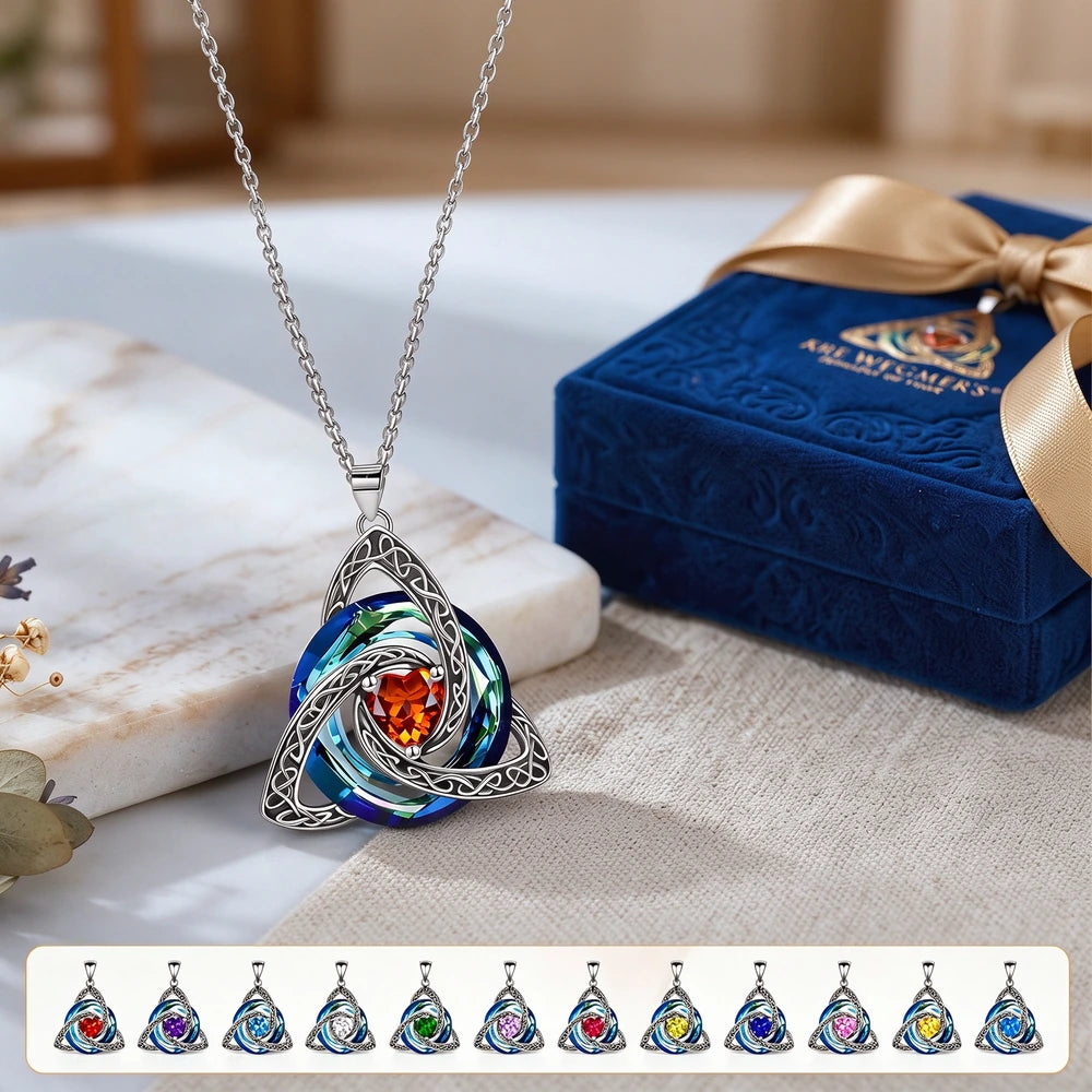 A silver Celtic knot triquetra pendant necklace with a central orange gemstone and swirling blue iridescent accents, displayed next to a blue gift box. A row of color variant pendants is shown at the bottom.