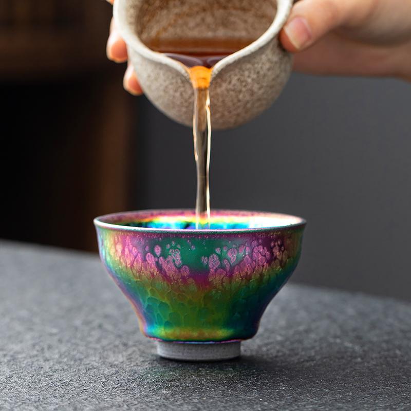 Peacock Plume Jian Zhan Tea Cup with vibrant iridescent glaze and golden floral detail, water being poured into handcrafted ceramic tea cup.
