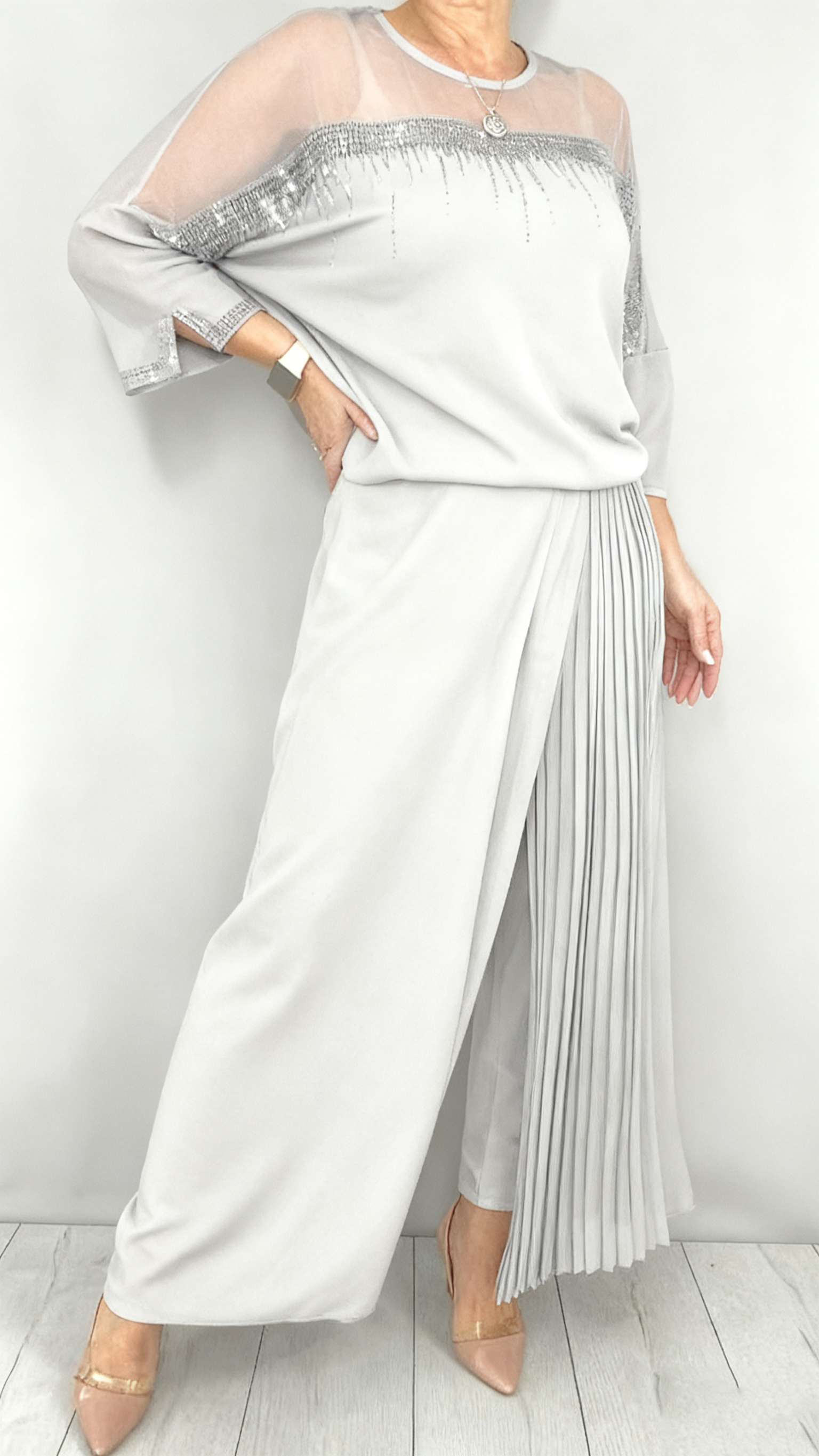 Garnitur z przezroczystym tiulem i cekinami na rękawach i dekolcie oraz plisowanymi panelami na spodniach.