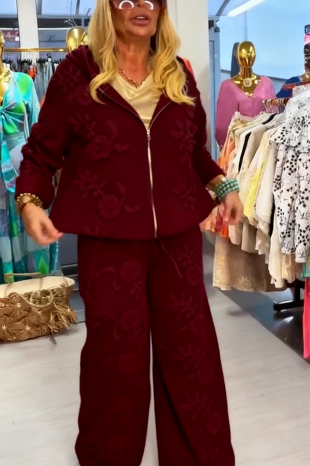 Damski kostium składa się z bluzy z kapturem ozdobionej eleganckim kwiatowym wzorem oraz szerokich spodni.