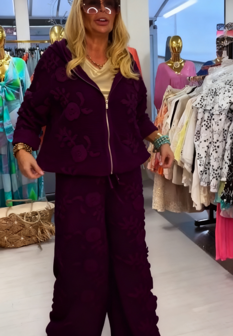 Damski kostium składa się z bluzy z kapturem ozdobionej eleganckim kwiatowym wzorem oraz szerokich spodni.