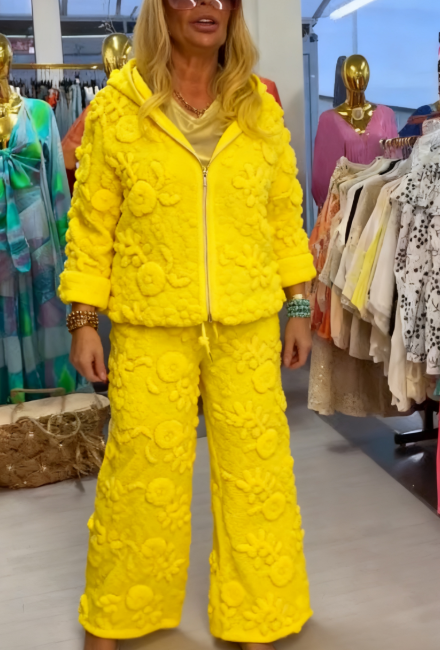 Damski kostium składa się z bluzy z kapturem ozdobionej eleganckim kwiatowym wzorem oraz szerokich spodni.