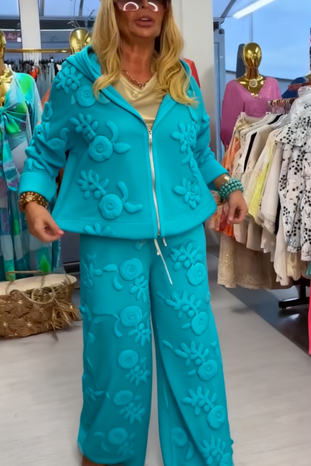 Damski kostium składa się z bluzy z kapturem ozdobionej eleganckim kwiatowym wzorem oraz szerokich spodni.