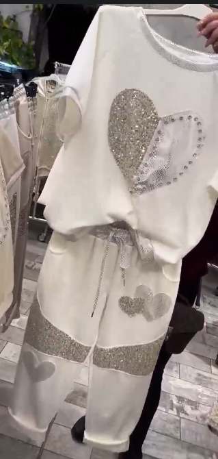 Prosty top z dekoltem w kształcie serca ozdobionym cekinami w połączeniu ze spodniami ozdobionymi serduszkami i cekinami.
