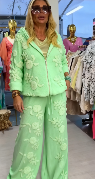 Damski kostium składa się z bluzy z kapturem ozdobionej eleganckim kwiatowym wzorem oraz szerokich spodni.