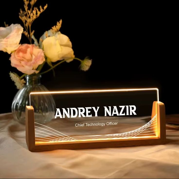A modern acrylic desk name plate illuminated with soft LED lighting, displaying the employee's name in glowing text on a sleek office desk.