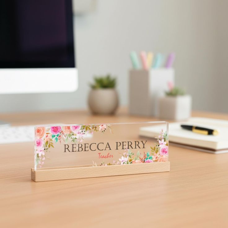 An elegant acrylic desk name plate adorned with delicate floral designs, featuring engraved text, perfect for a feminine or decorative office setting.