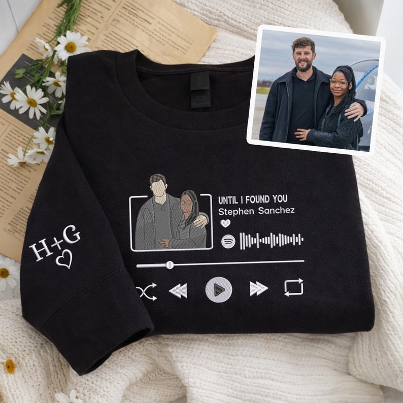 May include: Black sweatshirt with a custom design. The design includes a couple illustration, music player interface, and the text "UNTIL I FOUND YOU Stephen Sanchez". The left sleeve has embroidered initials "H+G" with a heart.