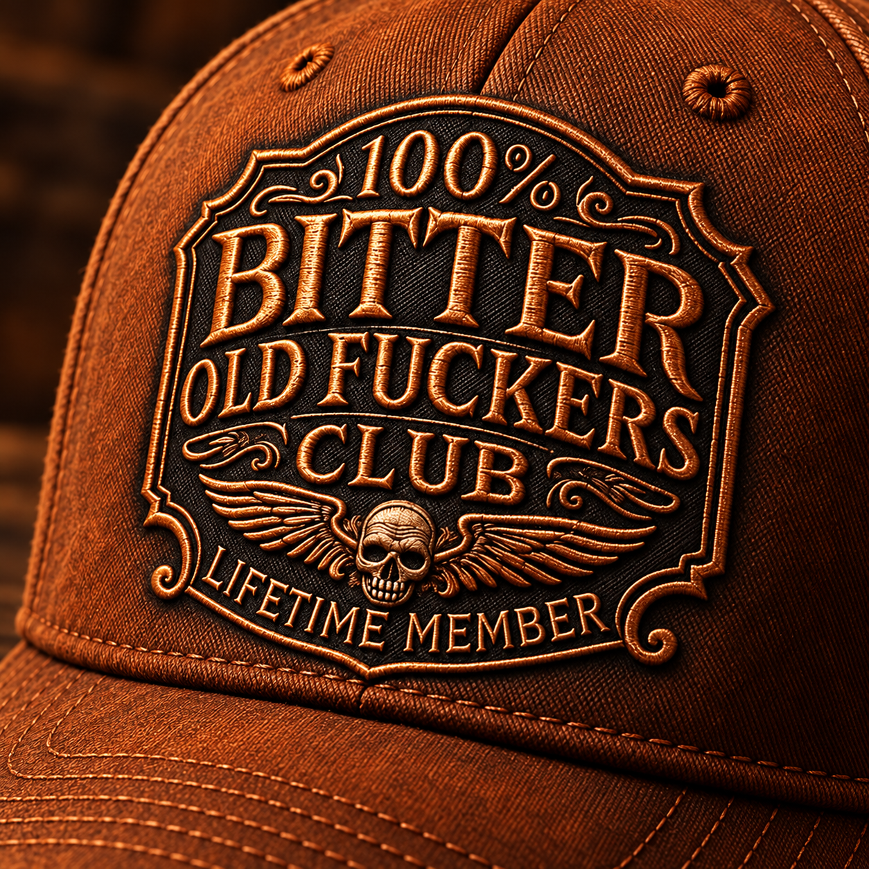 Close-up of copper-tone embroidered badge lettering, ornate border, winged skull and rust brown cap stitching
