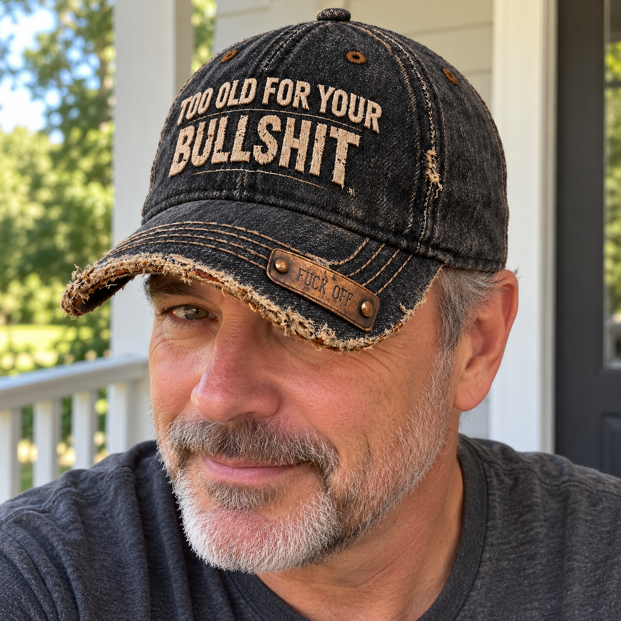 An adult man wearing the distressed black slogan cap with the copper-tone brim plaque visible