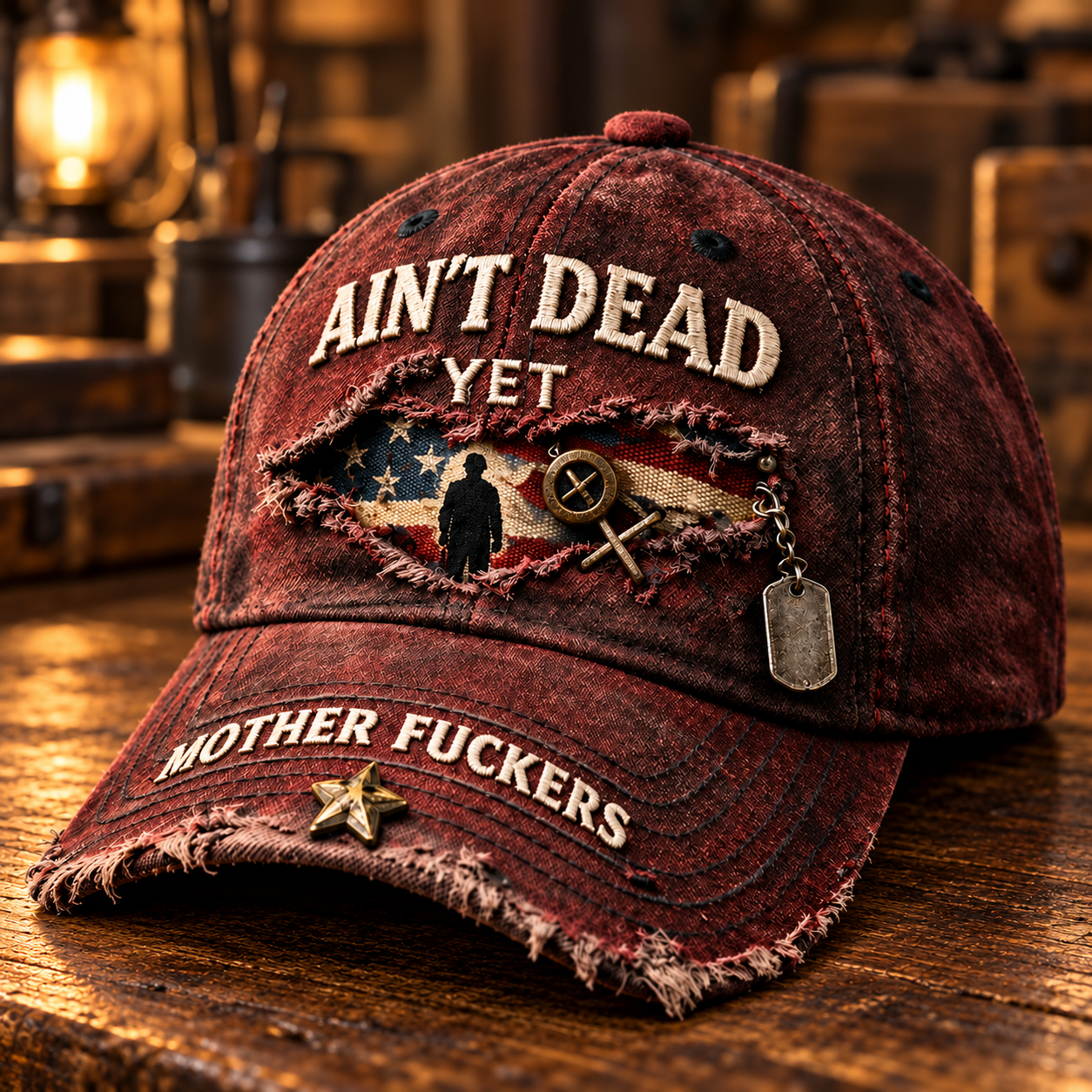 Weathered burgundy Ain&rsquo;t Dead Yet cap with flag-and-person panel, hanging silver dog tag, brim lettering and gold-tone star