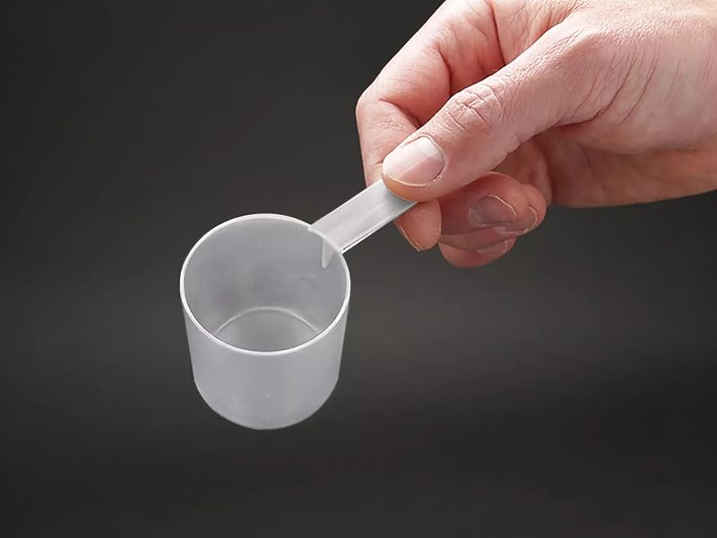 Tenere in mano un piccolo misurino in plastica trasparente su sfondo scuro.