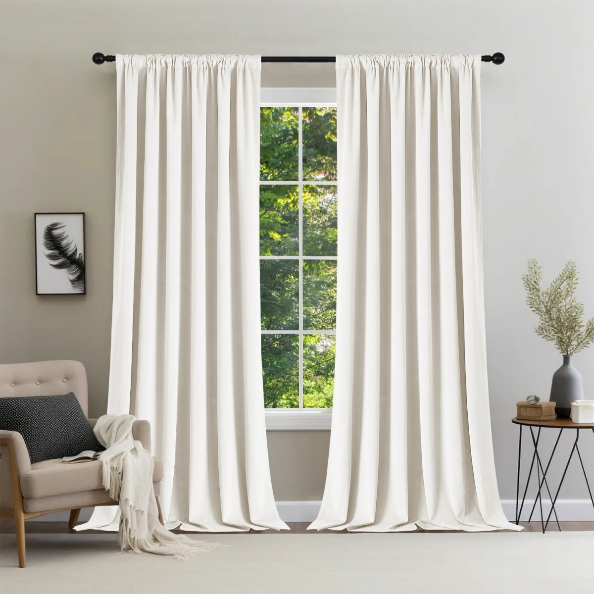 Two cream Joydeco velvet blackout curtains on rod, window with greenery. Room decor includes chair.
