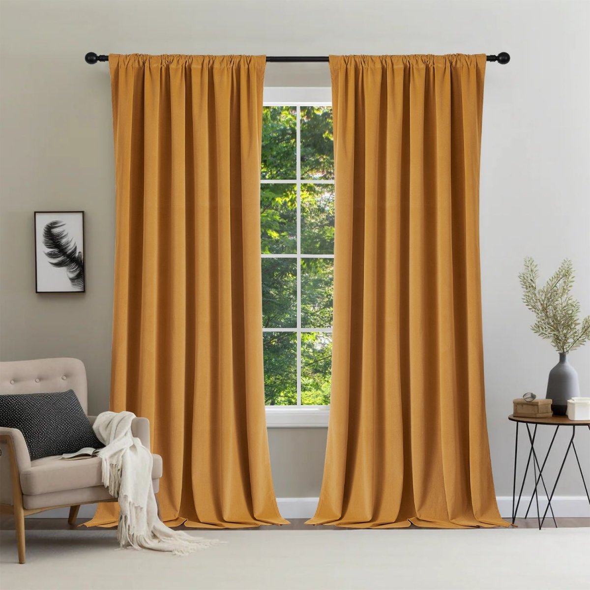 Two mustard-yellow Joydeco velvet blackout curtains on black rod, window with green trees, armchair with throw blanket.