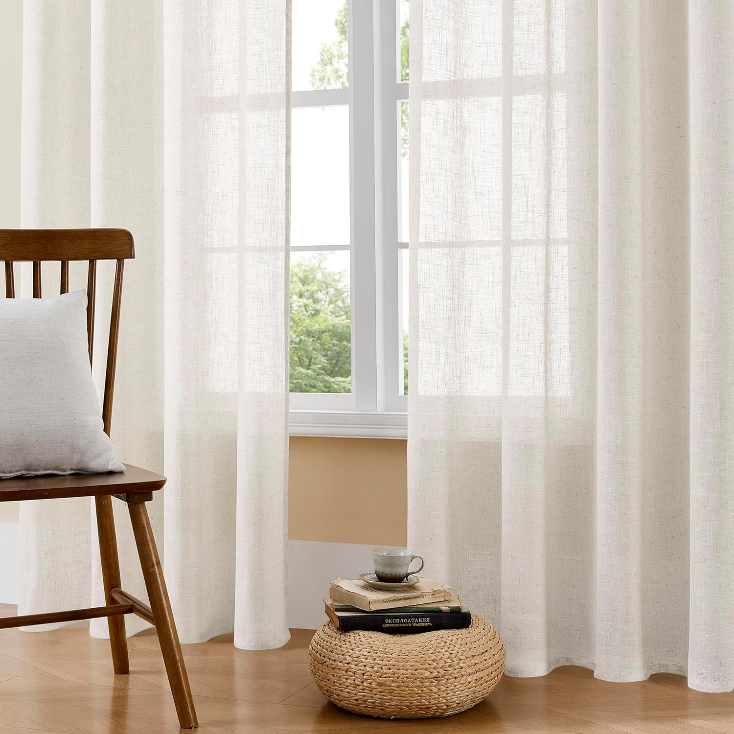 Two beige semi-sheer linen curtains with rod pockets filter sunlight on window near wooden chair.