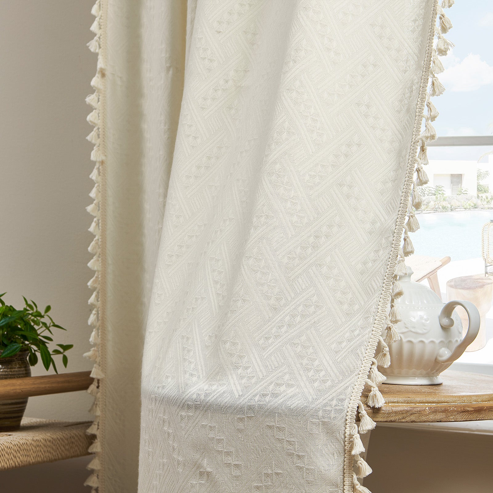 Close up of cream boho curtains with woven diamond pattern and cream tassel trim, showcasing soft fabric texture.