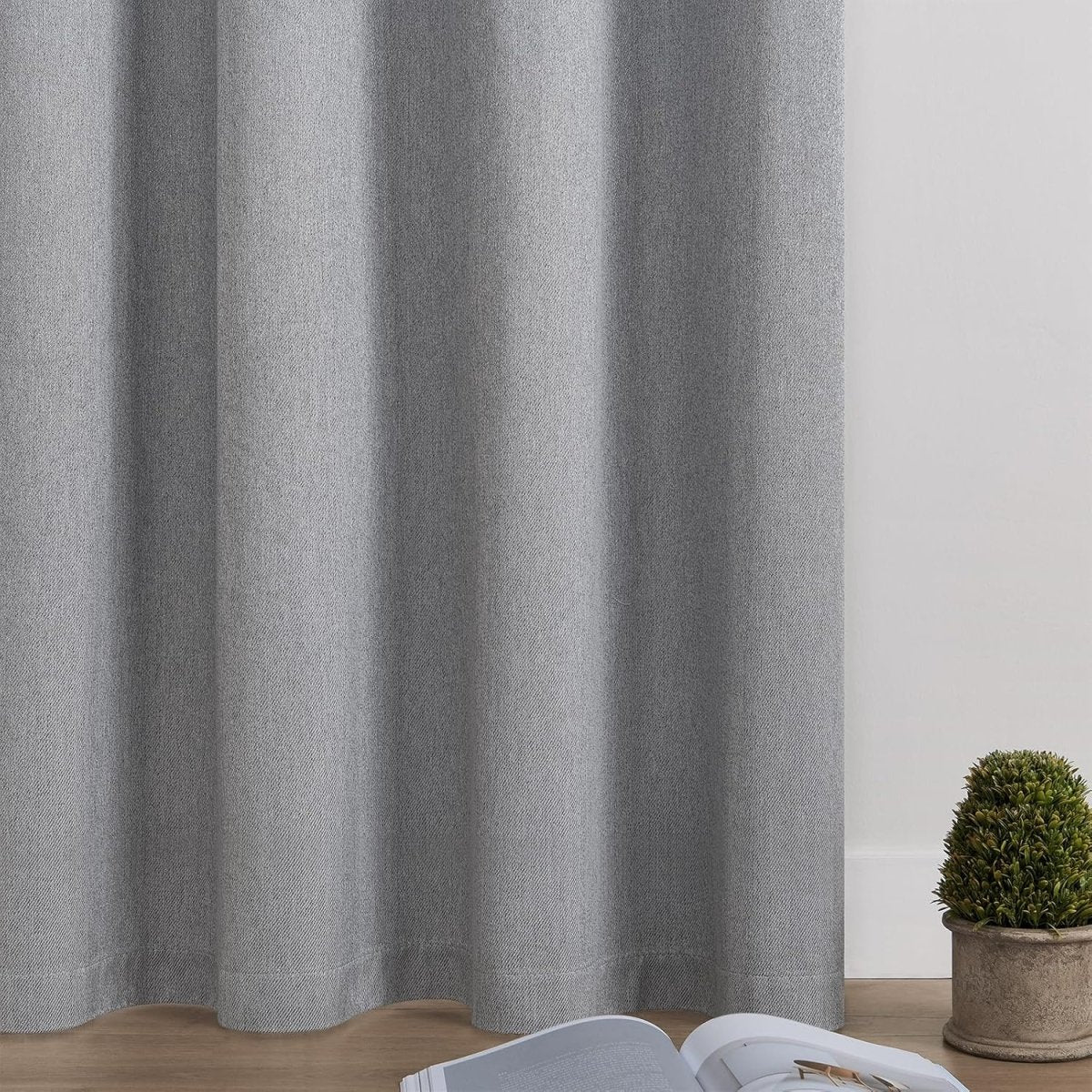 Light gray faux linen Joydeco blackout curtain panel texture and drape detail, with plant and book.