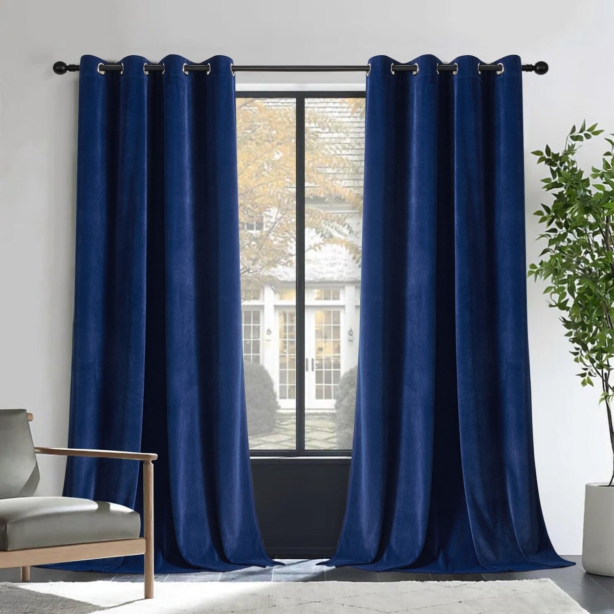 Two royal blue velvet blackout curtains with grommets on rod, framing window with house view. Includes armchair and plant.