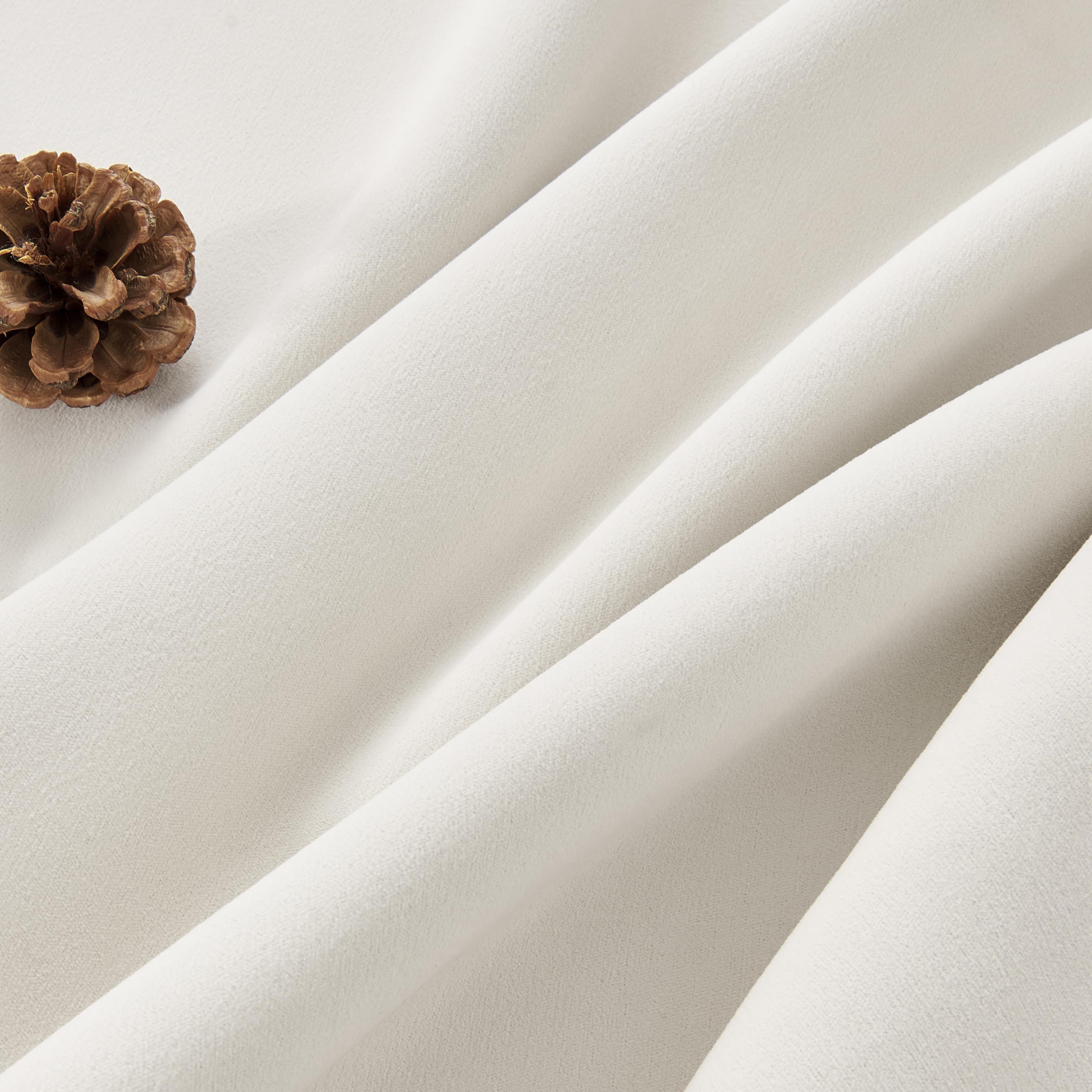 Cream velvet fabric texture close-up with pinecone, highlighting luxury blackout and thermal drapes.