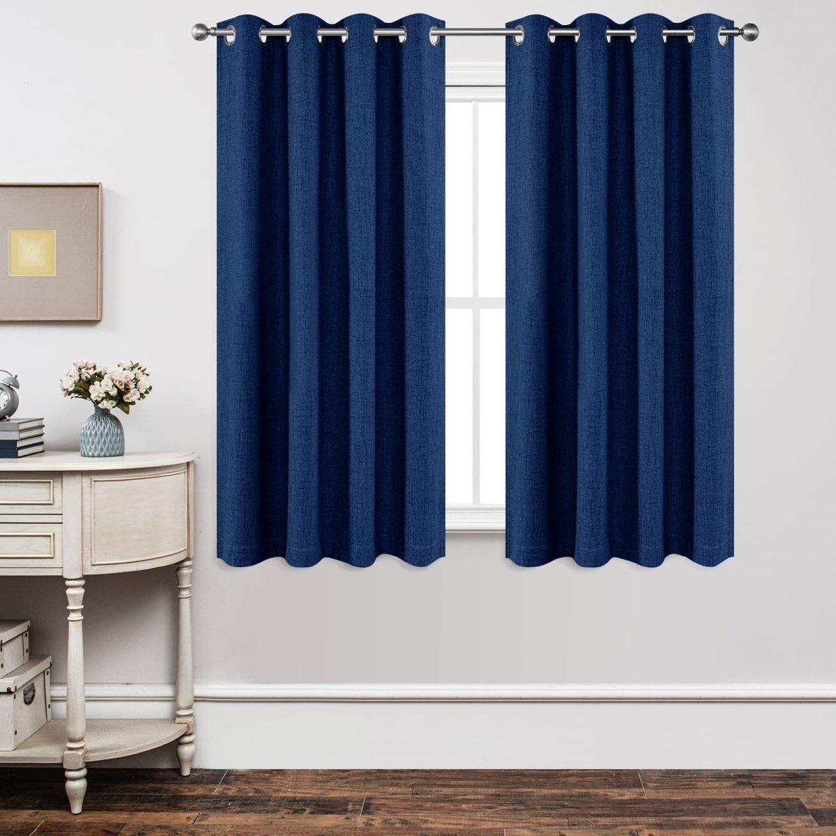Navy blue textured linen blackout curtains with metal grommets hang on silver rod over white window.