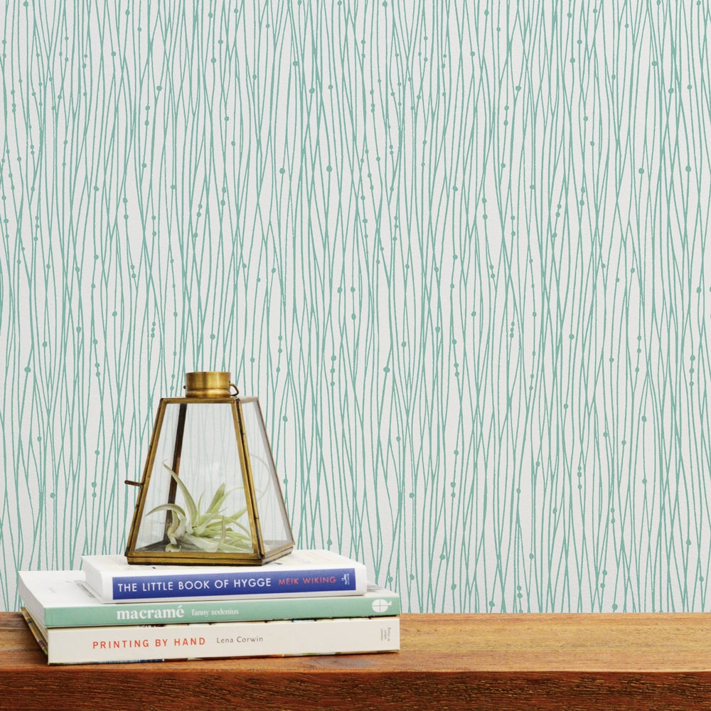 Tempaper's String of Pearls Peel And Stick Wallpaper in green behind a wood desk with three books on top.