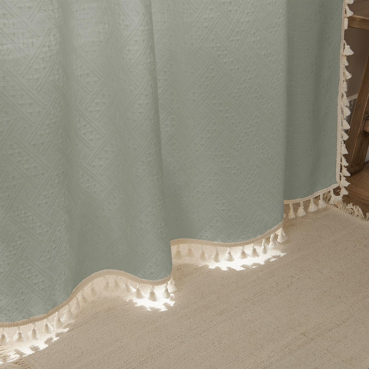 Close-up of sage green boho linen curtain with geometric pattern and cream tassels, showcasing texture.