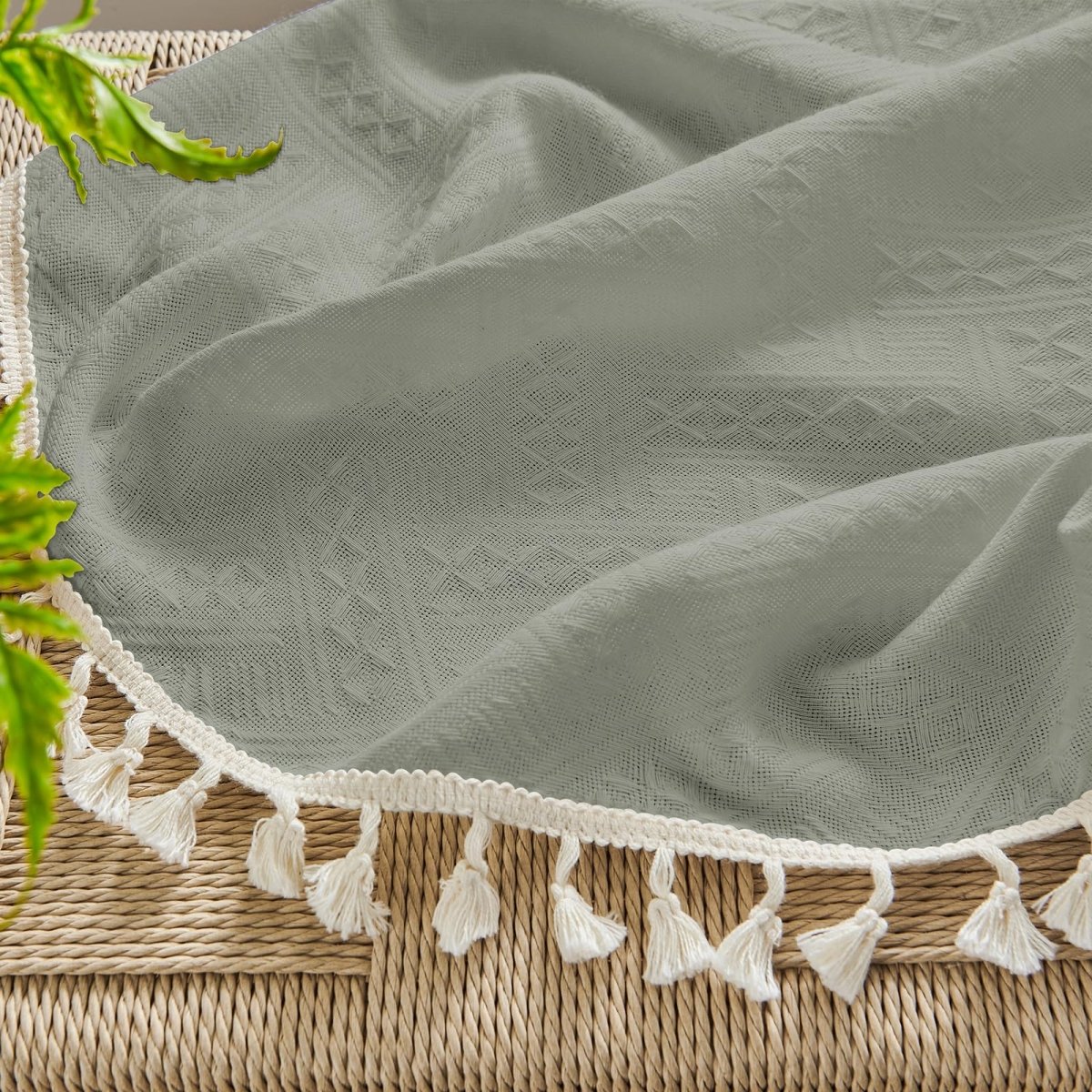 Close-up of grayish-green boho linen sheer curtain with geometric pattern and cream tassel trim, showcasing texture.