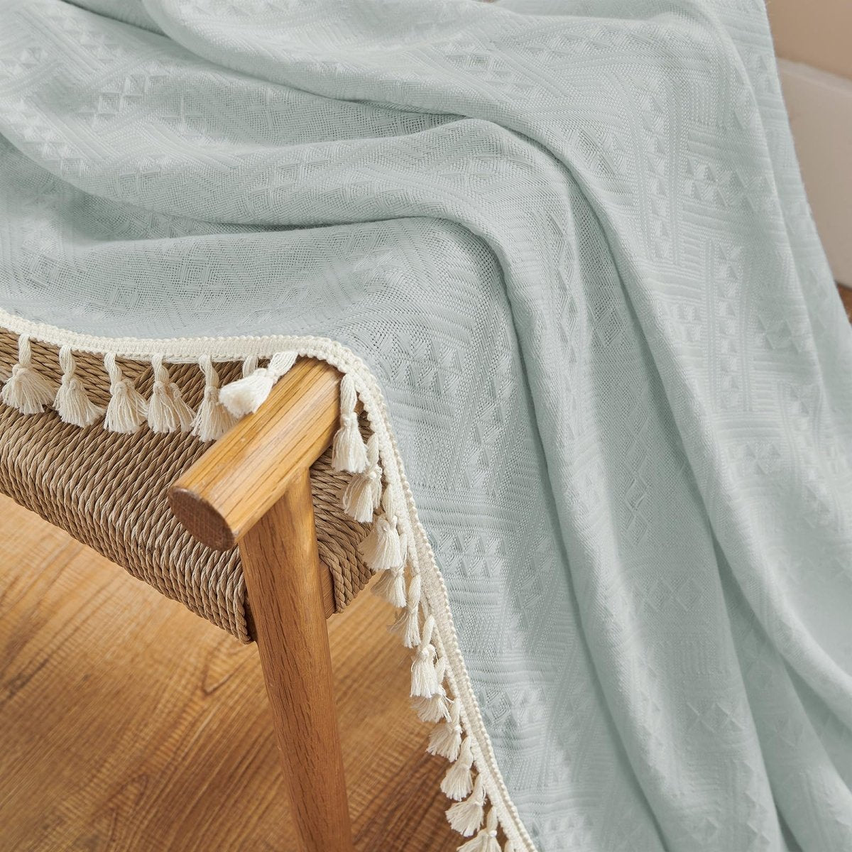 Light blue boho sheer linen curtain fabric close-up with geometric weave and cream tassels, draped on chair.