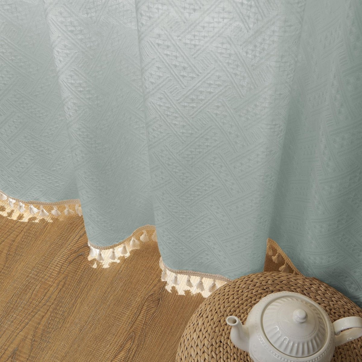 Close-up of ice blue linen sheer curtains with subtle geometric weave and cream tassels, showcasing boho farmhouse texture.