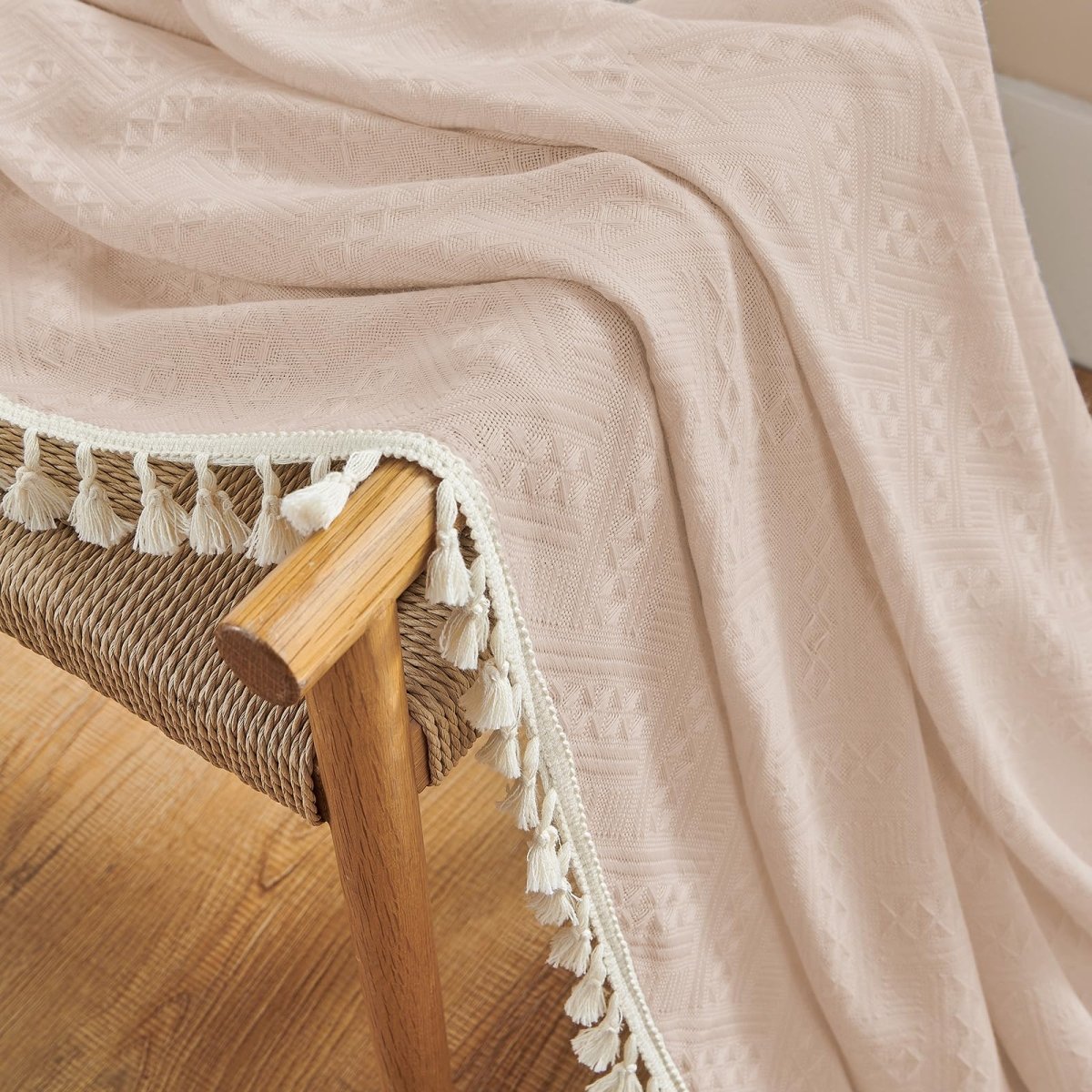 Close-up of pink boho linen fabric with geometric pattern and cream tassel fringe detail on a woven chair.