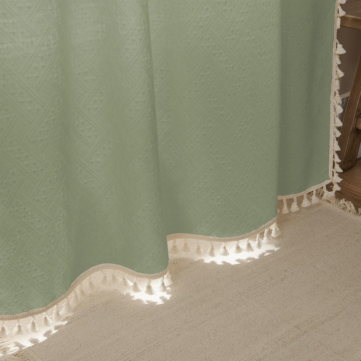 Boho sage green linen sheer curtain with diamond weave, cream braided trim, and tassels, on a farmhouse rug.