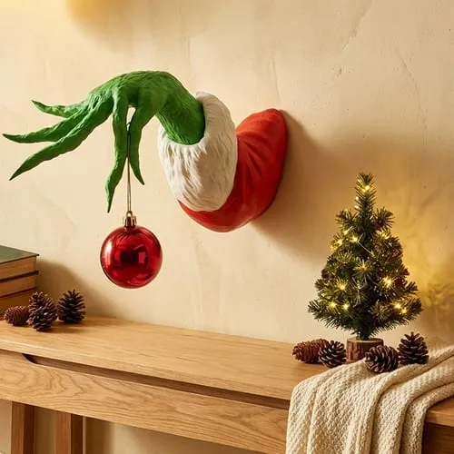 Green monster Christmas hand holding a red ornament on the wall