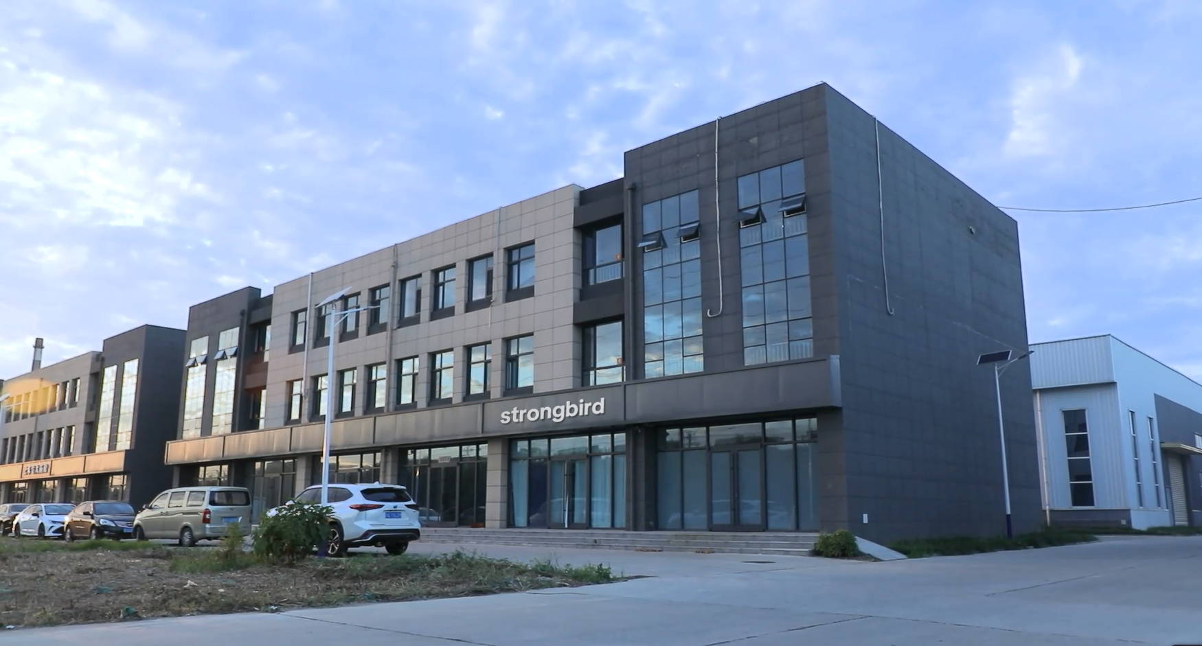 {"default":"Strongbird company office and production building exterior, showing company signage, architecture, and parked vehicles"}
