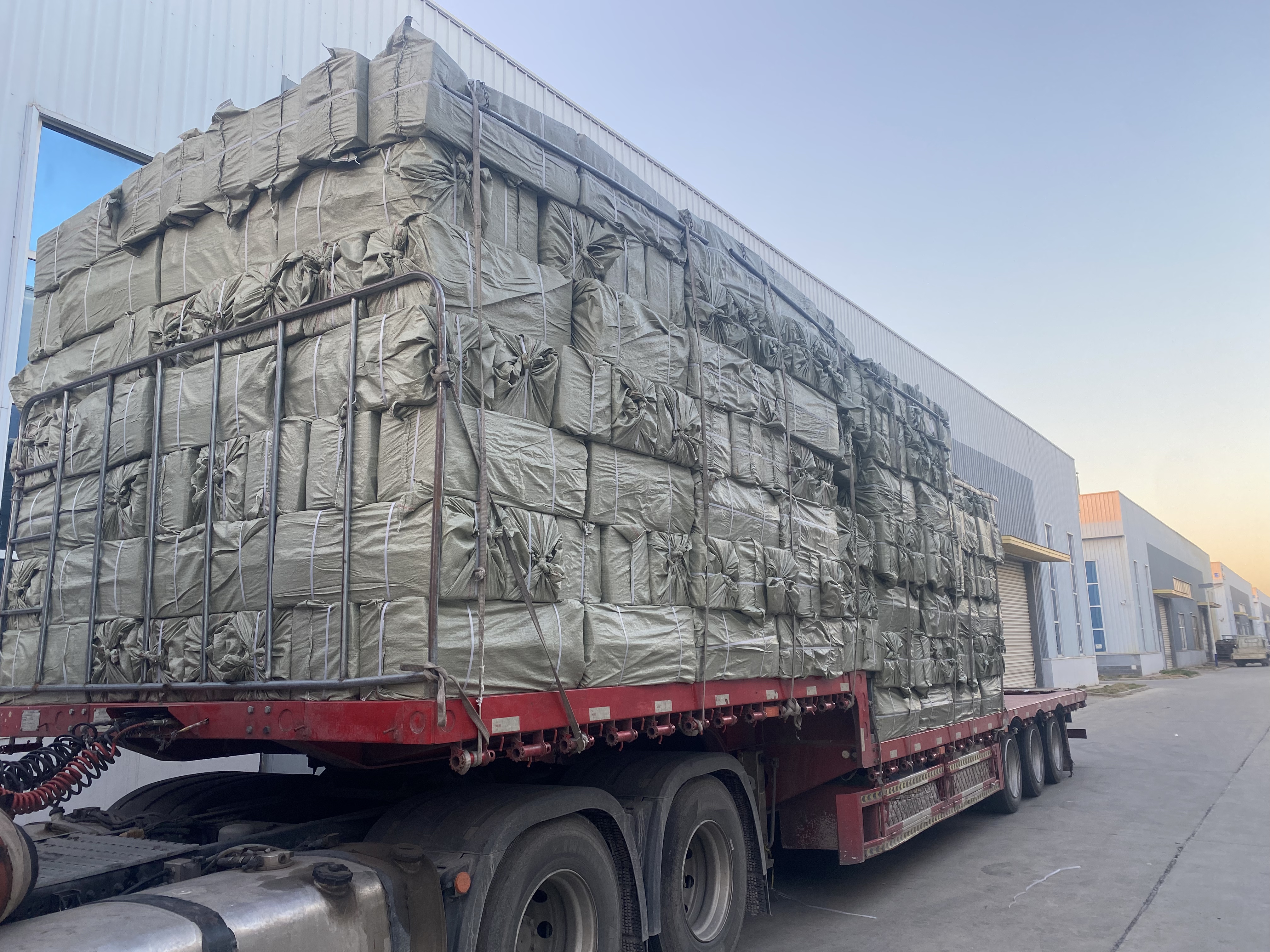 {"default":"Flatbed truck loaded with tightly wrapped cargo outside a factory, ready for shipment"}
