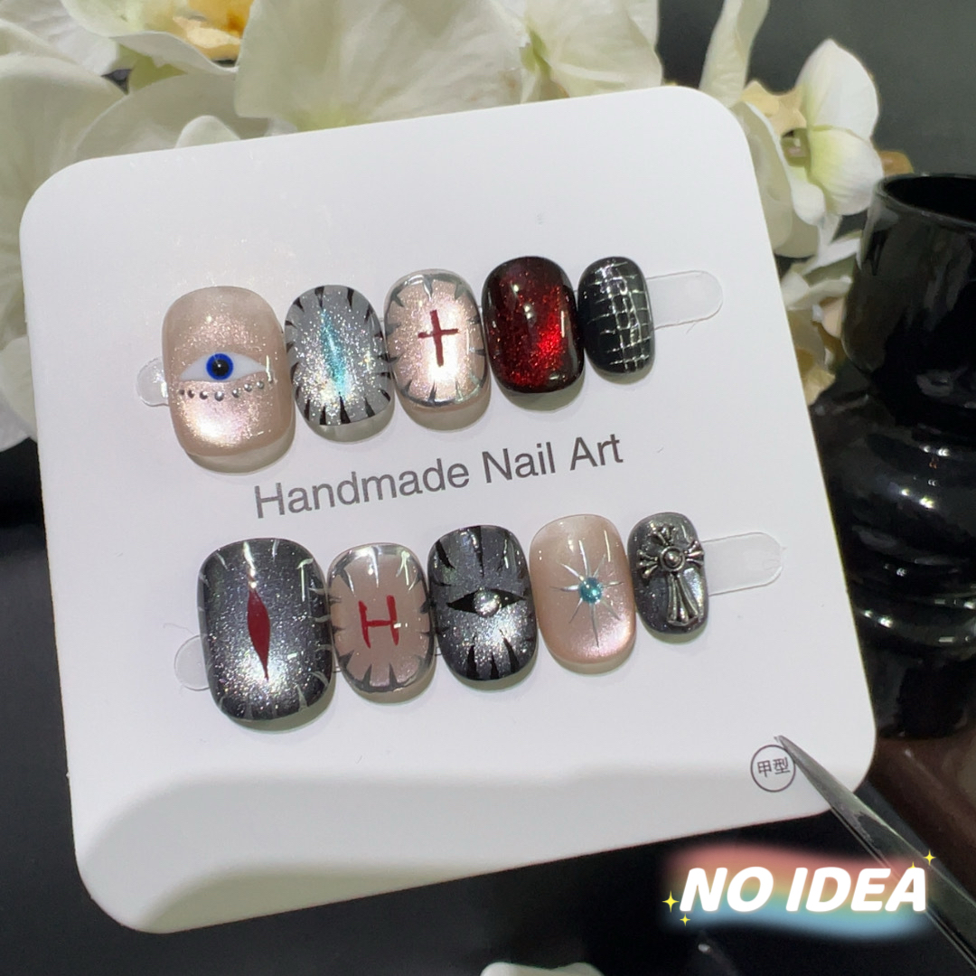 Dark red cat eye press on nails decorated with a blue eye charm, silver stars, and crosses.