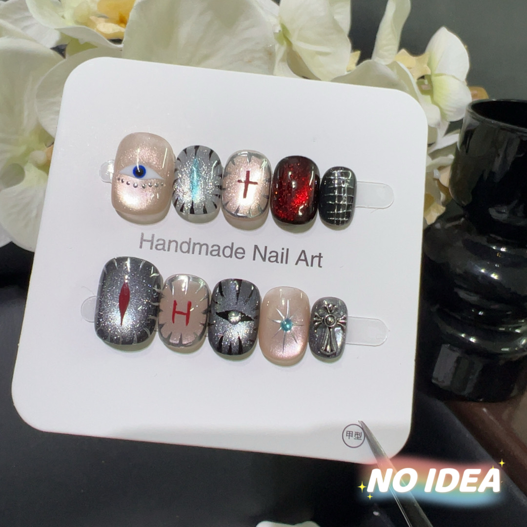 Dark red cat eye press on nails decorated with a blue eye charm, silver stars, and crosses.