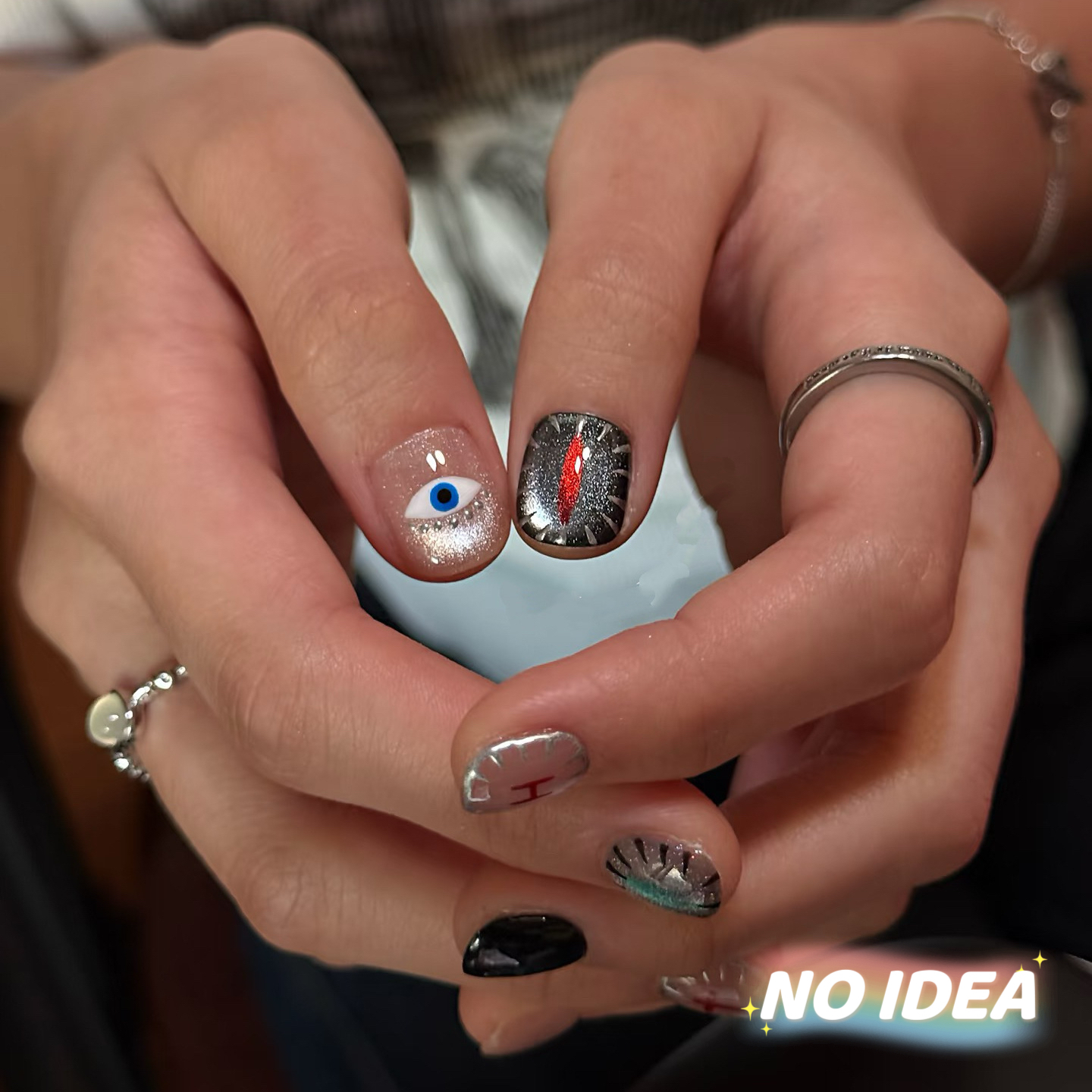 Dark red cat eye press on nails decorated with a blue eye charm, silver stars, and crosses.