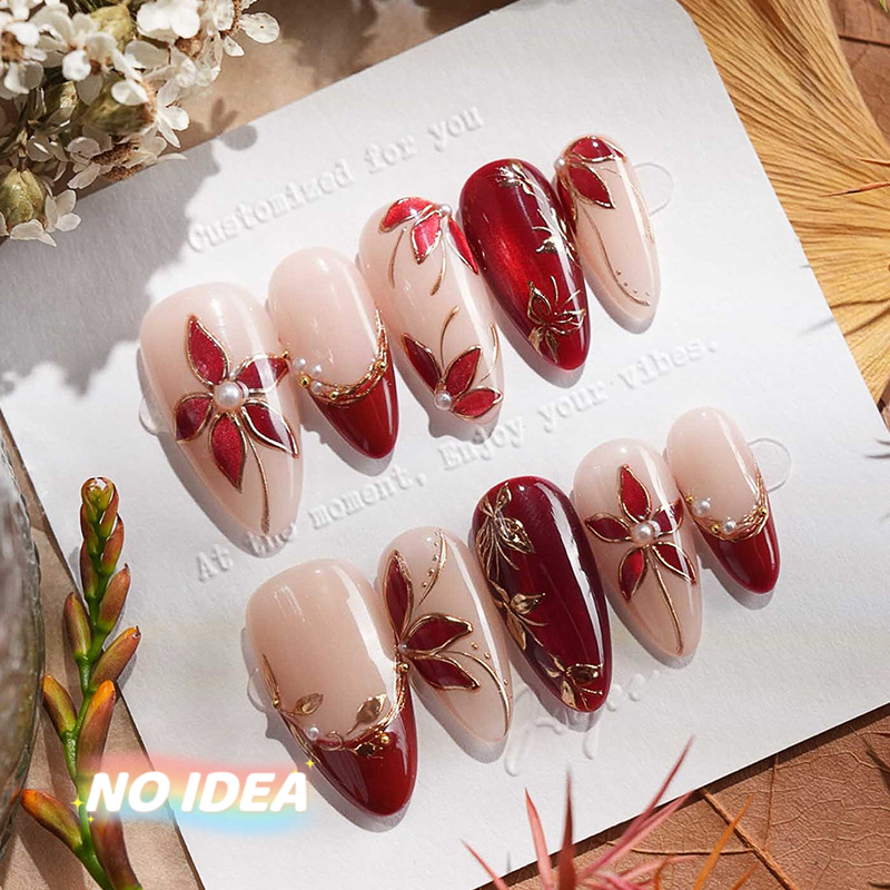 Set of short almond shaped press on nails in wine red with metallic silver floral designs, arrayed by size.
