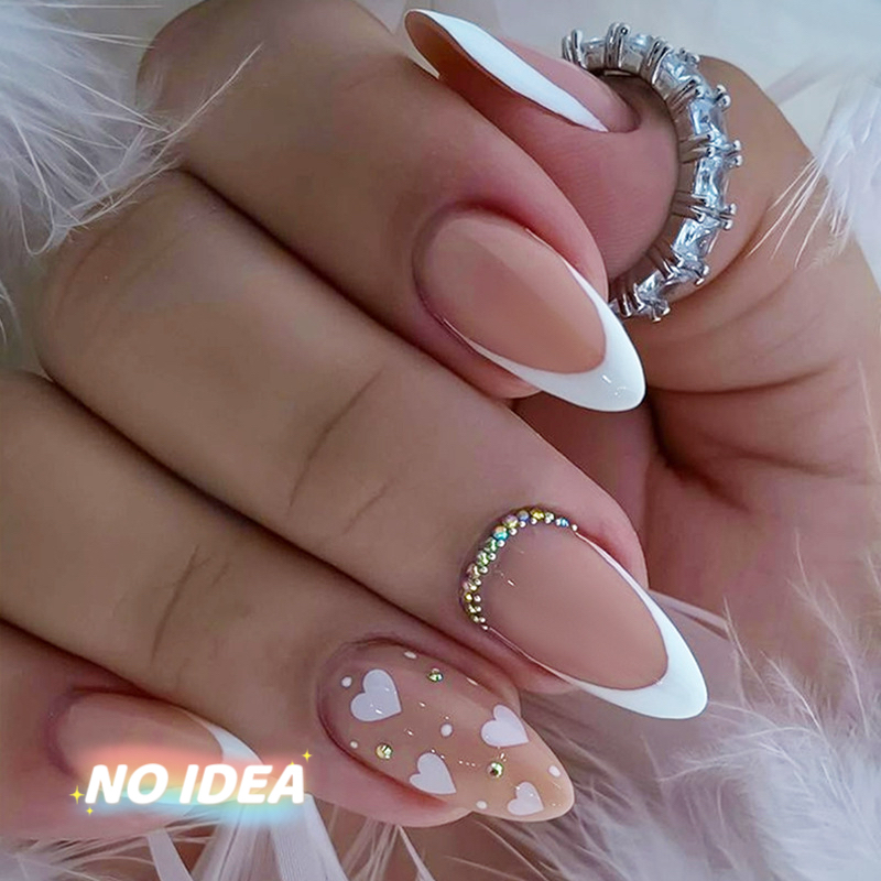 Almond shaped press on nails with a nude base, white French tips, and small white heart designs.