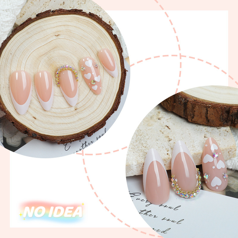 Almond shaped press on nails with a nude base, white French tips, and small white heart designs.